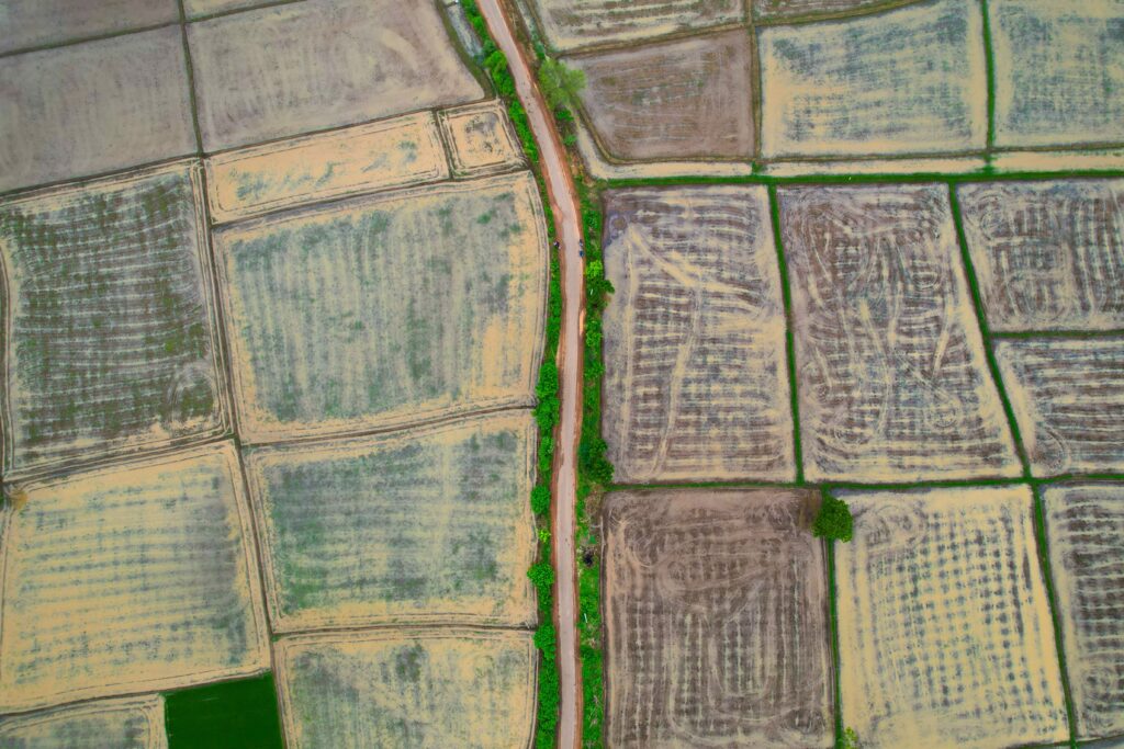 Aerial view of agricultural fields divided into separate parcels by field boundaries and a rural road. | Photo by Raj Manohar via Pexels